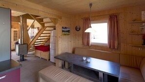 L'interno di una baita in legno con un'area pranzo, una scala e una finestra con tende.