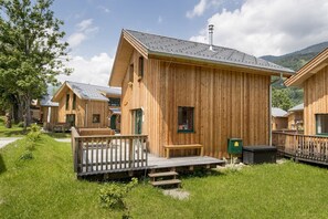 A row of wooden cabins with a deck and a small bench, surrounded by greenery and mountains. - Chalet with e-charging station (Kreischberg Murau)
