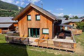 A wooden chalet with a deck, outdoor seating, and a mountain backdrop. - Pleasant chalet with sauna (Kreischberg Murau)