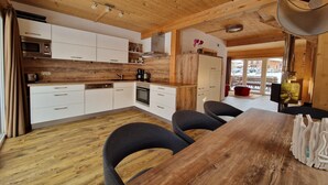 A modern kitchen with wooden cabinets, a dining area with a wooden table and chairs, and a view of the outdoors.