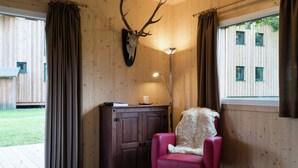 A room with a wooden interior, a mounted deer skull on the wall, a red armchair, and a floor lamp.
