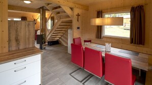 A wooden interior with a staircase, a dining area with red chairs, and a cross on the wall.