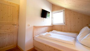 Une petite pièce aux murs lambrissés, avec un lit simple, un téléviseur fixé au mur et une fenêtre.