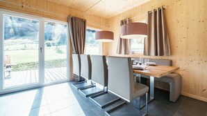 Un espace de repas moderne avec une table et des chaises en bois, de grandes fenêtres avec des rideaux et une vue sur un jardin.