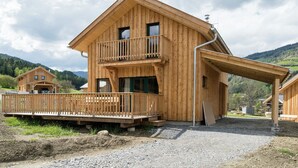 A wooden chalet with a balcony, a covered porch, and a gravel driveway.