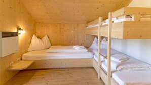 A wooden cabin with bunk beds, a small bedside table, and a wall-mounted heater.