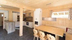 A wooden interior with a kitchen, dining area, and a window with curtains.