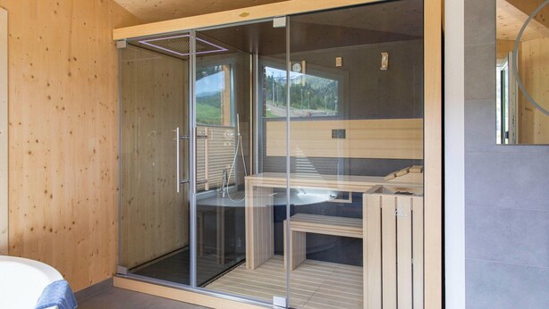 Un baño moderno con cabina de ducha de vidrio, bancos de madera y vistas exteriores.