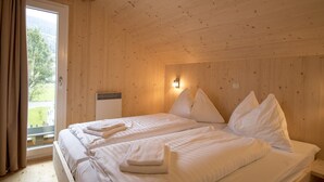 Una habitación de cabaña de madera con dos camas, una ventana con cortinas y una lámpara fijada a la pared.