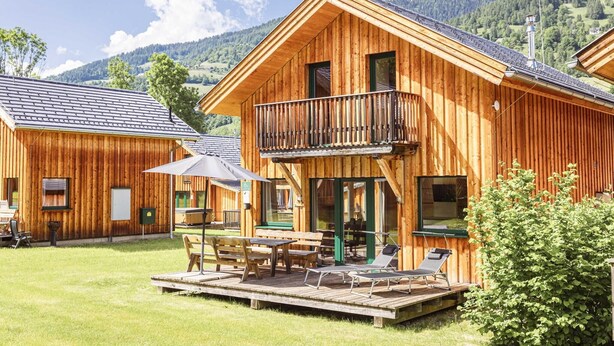Una cabaña de madera con balcón, mobiliario exterior y vistas a las montañas circundantes.