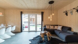 Un interior moderno con techo de madera, zona de comedor con sillas blancas, alfombra de cuero negro y sofá gris.