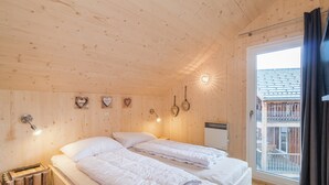 Un dormitorio tipo cabaña de madera con dos camas, una ventana con cortinas y vistas a un balcón.