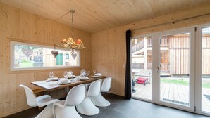 Un comedor moderno con una mesa de madera, sillas blancas y una araña.