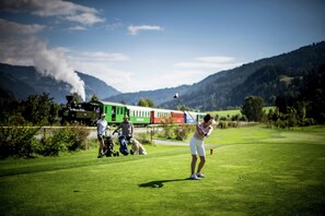 Campo de golf con un tren al fondo y montañas.