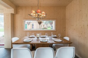 Un comedor con mesa de madera dispuesta para seis personas, sillas blancas y una araña.