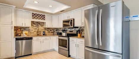 A modern kitchen with white cabinets, a stainless steel refrigerator, a microwave, and a dishwasher.