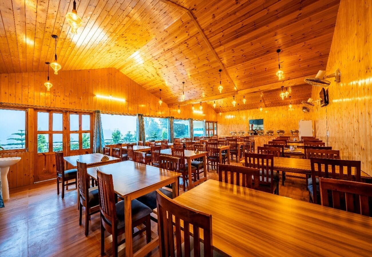 Un comedor amplio con mesas y sillas de madera, ventanas grandes y un techo alto.