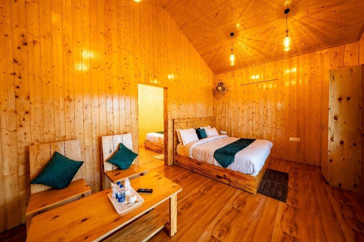 A wooden cabin room with two beds, a table, and a bench.