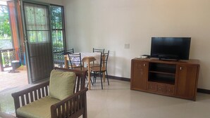 A living room with a sofa, a dining table with chairs, a television on a wooden cabinet, and a sliding glass door leading to an outdoor area. - House for rent in Hua Hin for wintering 180 days visa (Hua Hin)