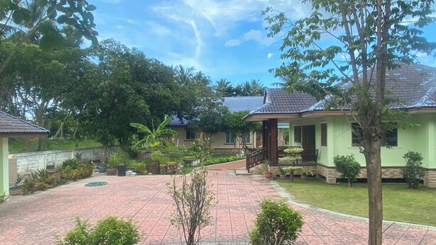 A residential area with a paved courtyard, a small bridge, and a house with a tiled roof. - House for rent in Hua Hin for wintering 180 days visa (Hua Hin)