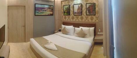 Habitación de hotel ordenada con cama, mesita de noche y televisor instalado en la pared.