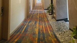 A hotel hallway with a colorful carpet, marble walls, and a potted plant.