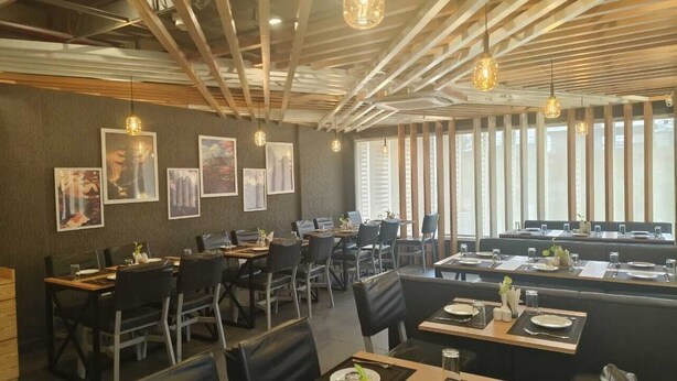 A restaurant with a modern interior, featuring wooden ceiling beams, pendant lighting, and framed artwork on the walls.