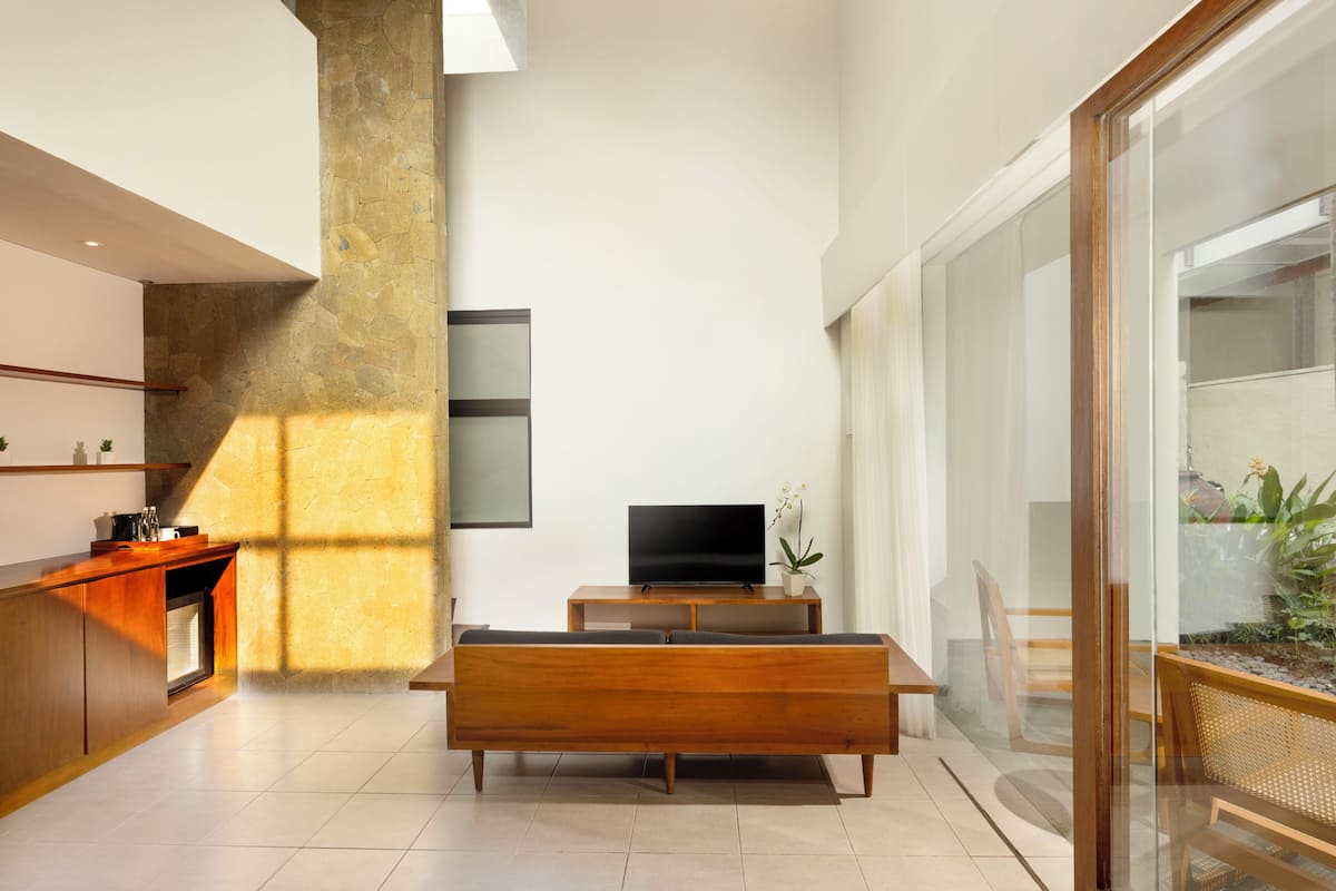 A modern living room with a wooden bench, a flat-screen TV, and a glass partition.
