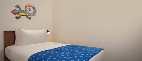 Siististi pedattu sänky, jossa on sinikuvioinen päiväpeite, valkoinen tyyny ja värikäs seinäkoriste.