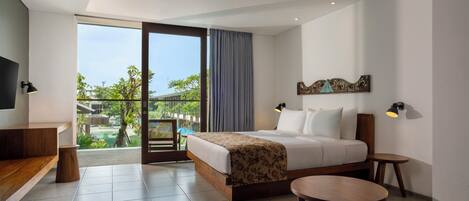 A modern hotel room with a large bed, a desk, a small table, and a balcony with a view of greenery and buildings.