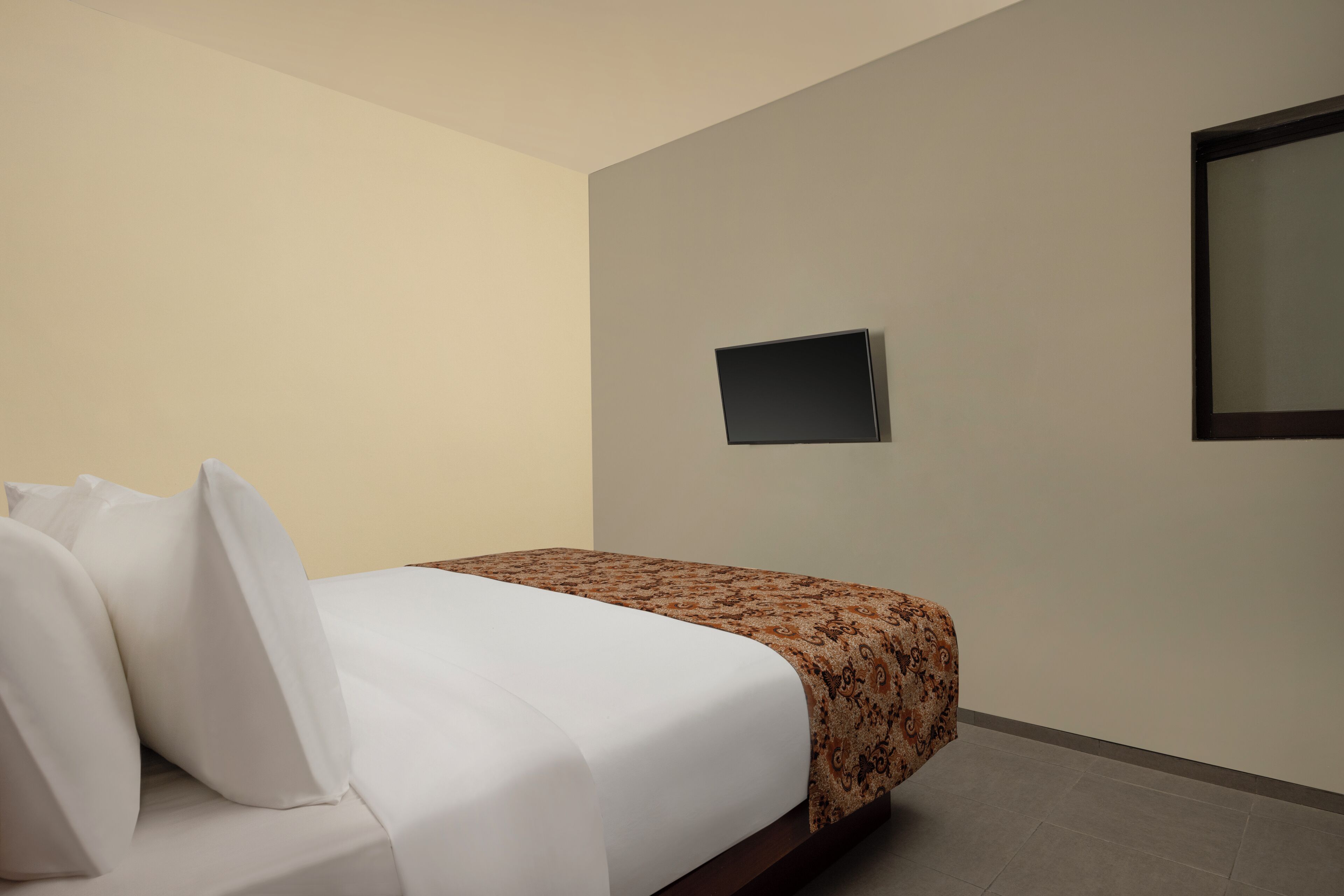 A hotel room with a bed, a flat-screen TV mounted on the wall, and a window.