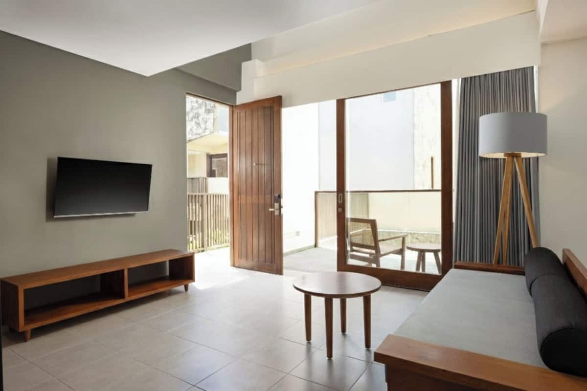 A modern living room with a flat-screen TV, wooden furniture, a sofa, and a balcony with a view.