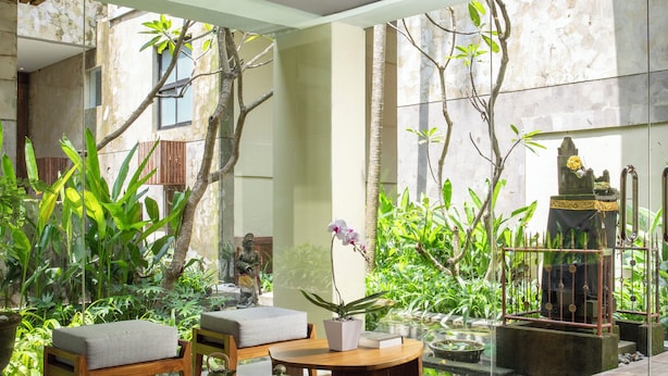 A modern interior with wooden furniture, a glass partition, and a view of greenery outside. - Dialoog Seminyak (Keroboken Kelod)