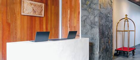 A reception desk with two laptops, a wooden wall, a stone pillar, and a gold-framed cart.