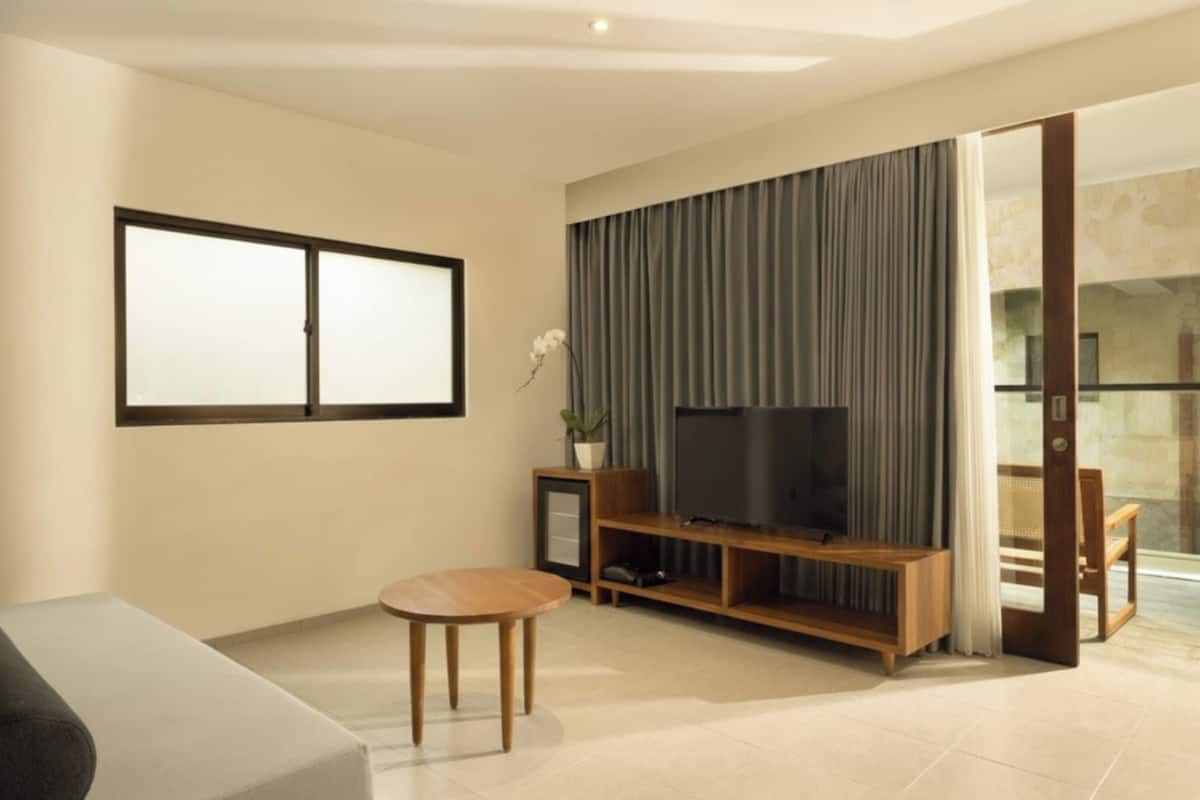 A modern living room with a flat-screen TV, wooden entertainment unit, and a sliding glass door leading to a balcony.