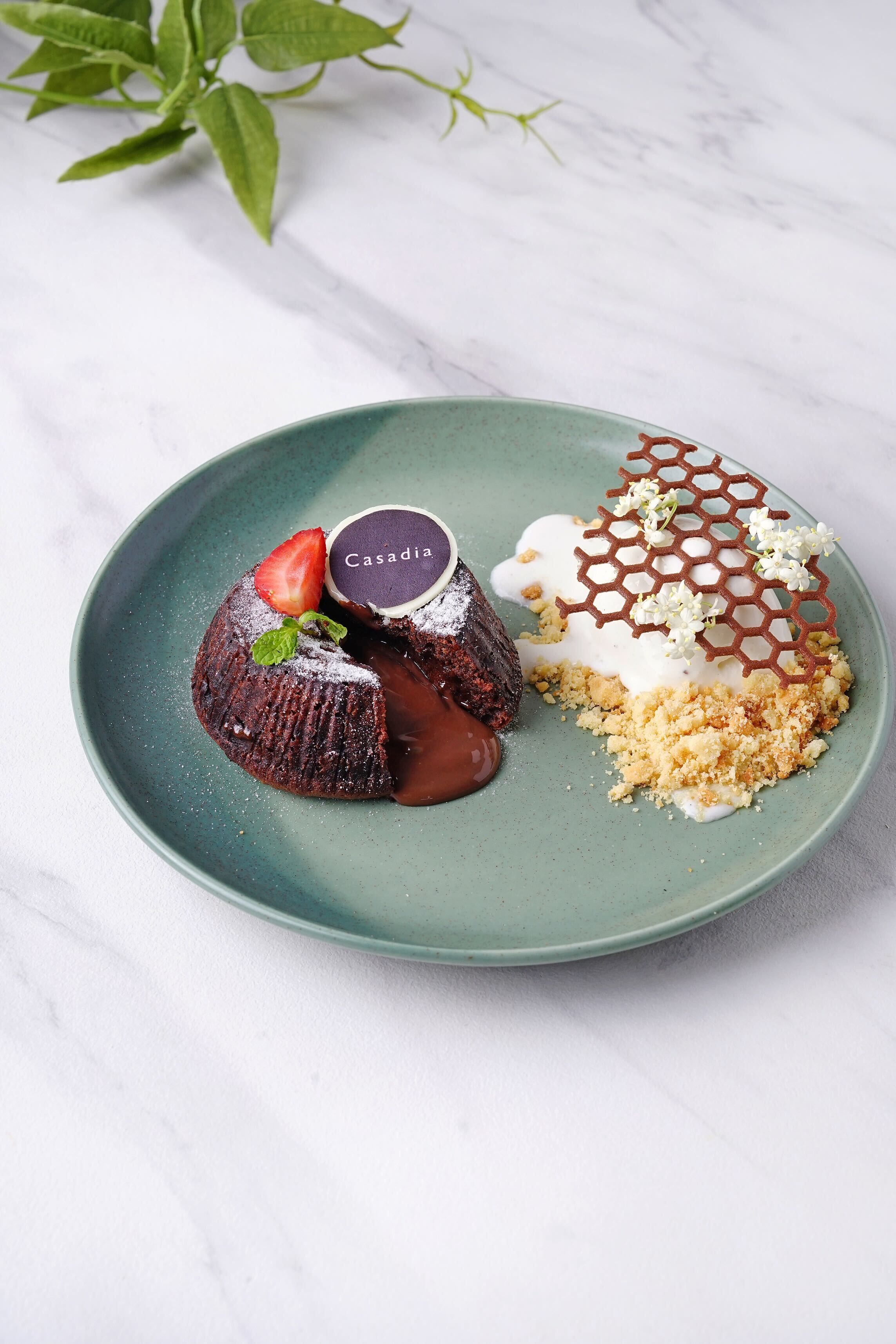 Une assiette de dessert avec un fondant au chocolat, une boule de glace et un dessert au miel d’abeilles, le tout présenté sur une assiette verte.