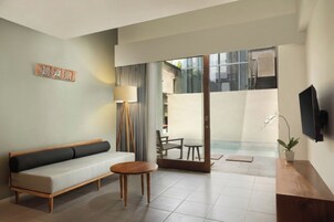 Un salon moderne avec un canapé, une petite table ronde, une lampe et un téléviseur fixé au mur.