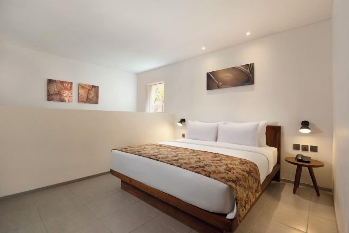 A modern hotel room with a large bed, two wall-mounted lamps, and artwork on the walls.