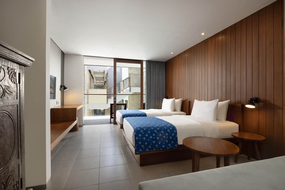 A hotel room with two beds, a sofa, a small table, and a view of the outside.