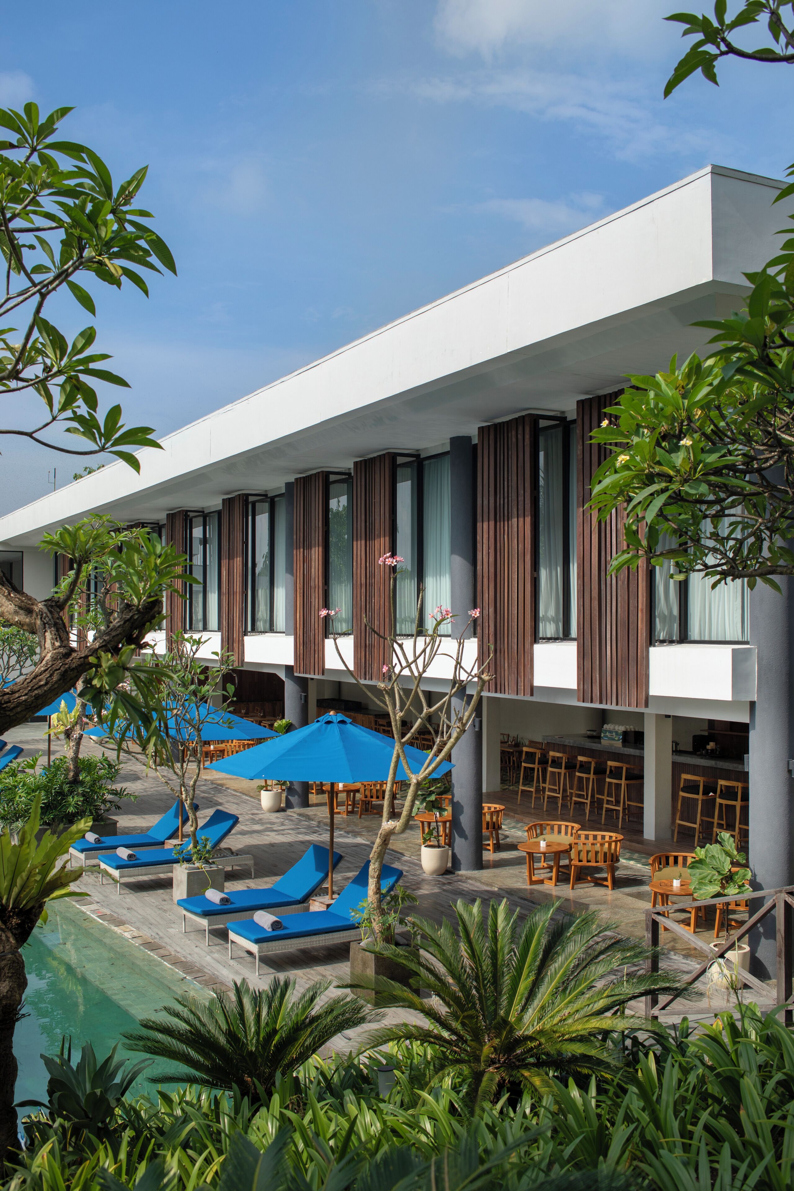 A modern hotel with a pool area, lounge chairs, and wooden tables.