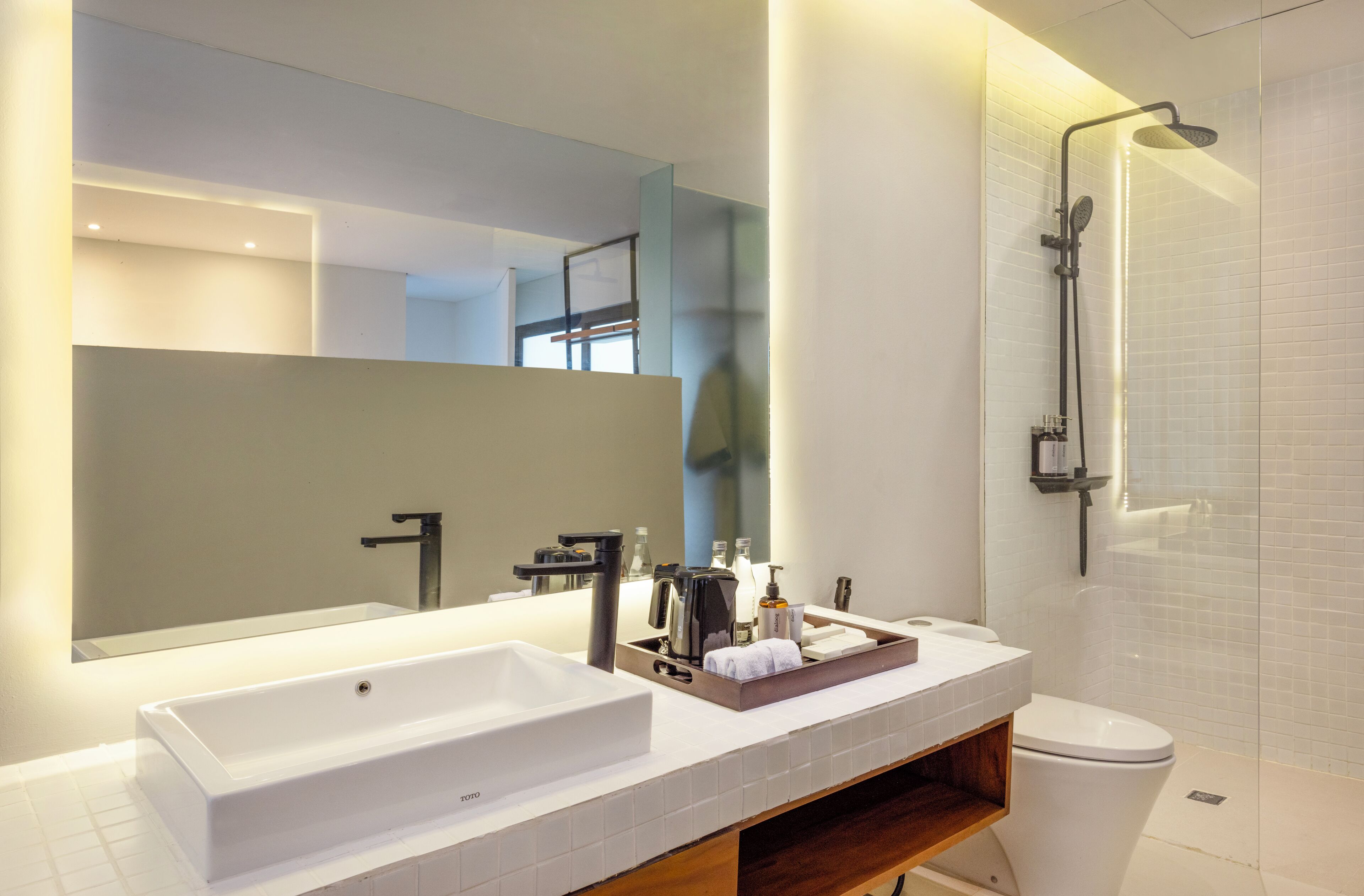 A modern bathroom with a large mirror, a white sink, a shower, and a toilet.