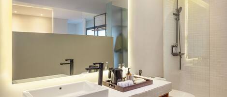 Un baño moderno con un espejo grande, un lavamanos blanco, una ducha y un inodoro.