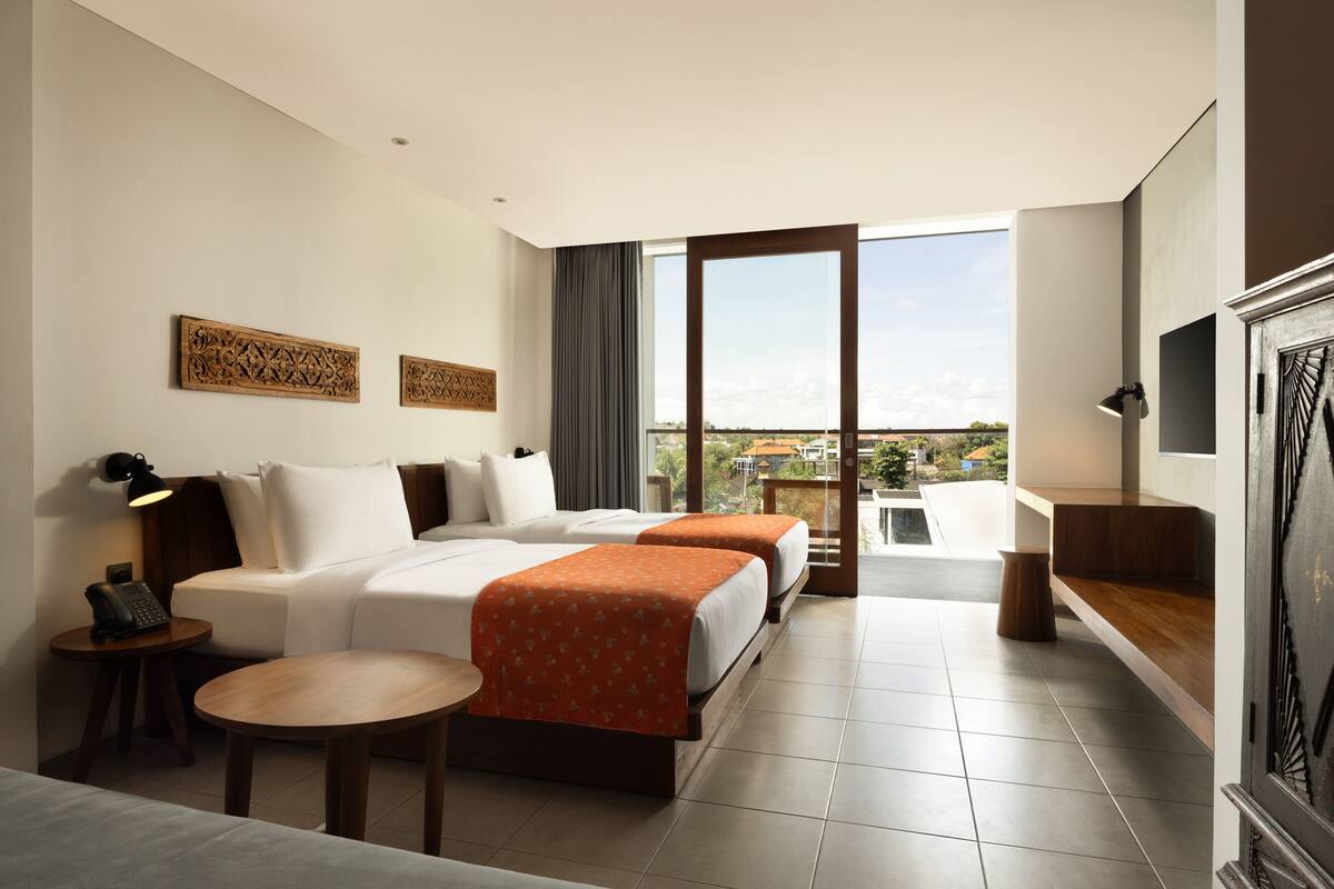 A hotel room with two beds, a desk, a chair, a TV, and a balcony with a view.