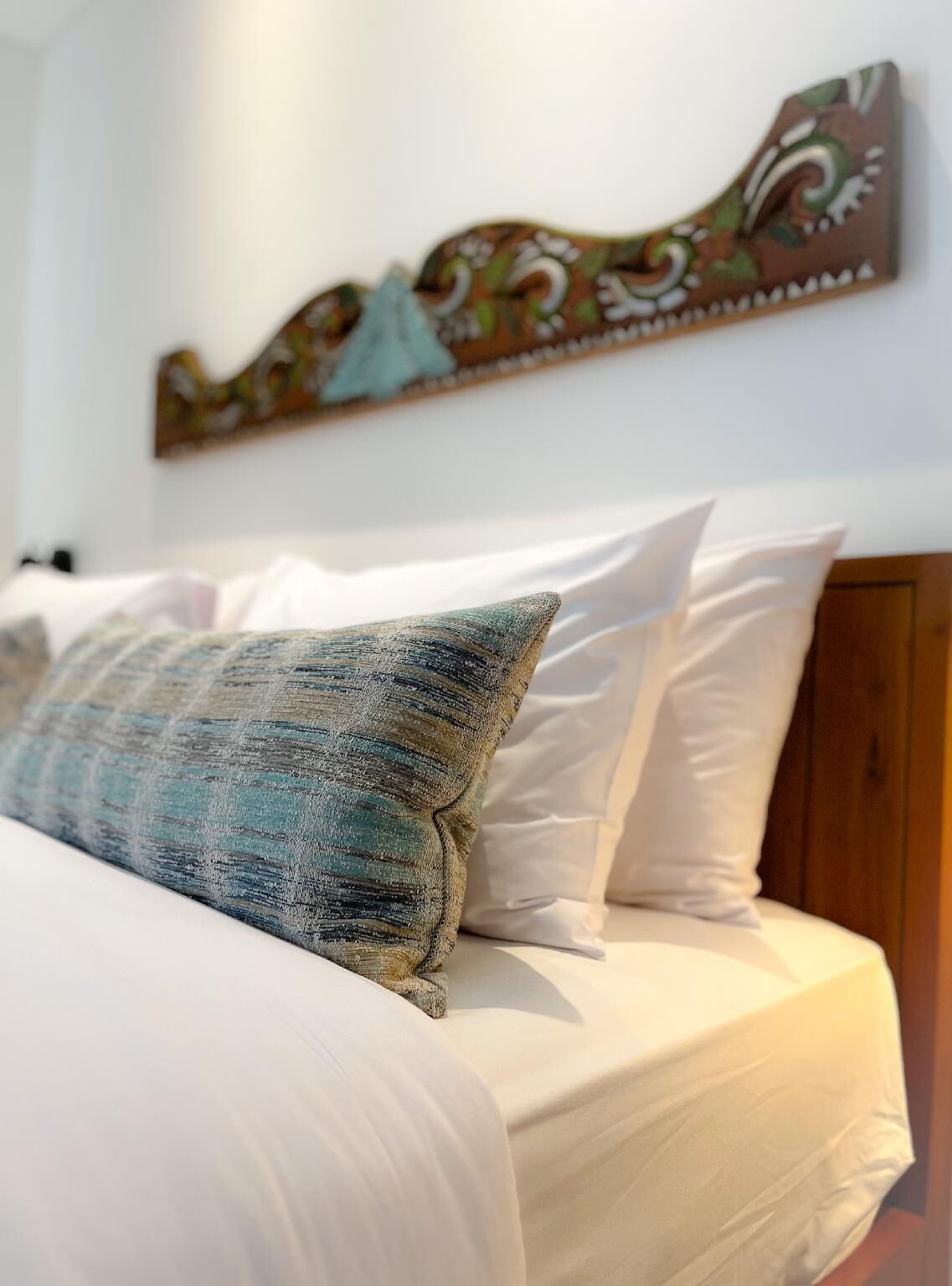Una cama con ropa de cama blanca y una única almohada decorativa.
