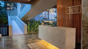 A modern reception area with a concrete counter, wooden paneling, and a stone accent wall. - Dialoog Seminyak (Keroboken Kelod)