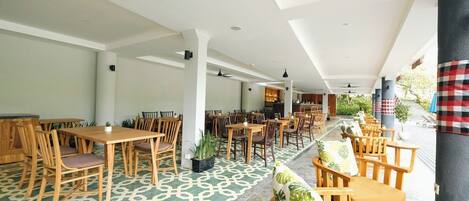 A spacious indoor area with multiple wooden tables and chairs, a patterned floor, and a view of the outside.