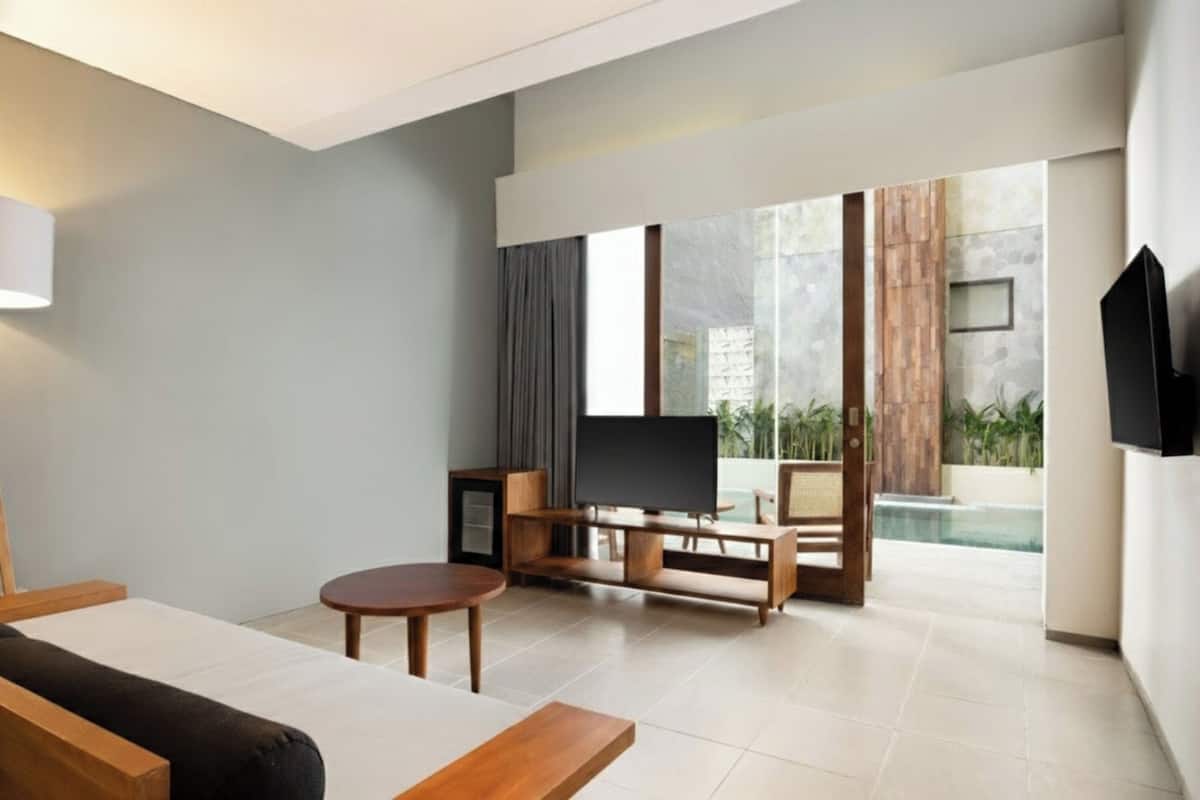 A modern living room with a flat-screen TV, wooden furniture, and a large window overlooking a pool.