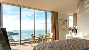 Habitación de hotel moderna con una cama grande, una mesa de comedor con sillas y vista al mar.