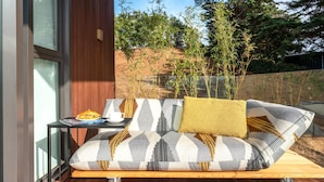 Un área de estar exterior moderna con un sofá, una mesita y una bandeja con comida y bebida.