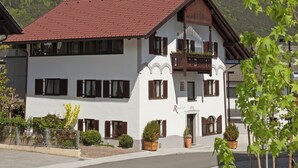 A two-story building with a red-tiled roof, white walls, and wooden balconies. It features multiple windows with shutters and a small garden area with potted plants. - Cozy vacation apartment and perfect base in the heart of Tyrol (Inzing)